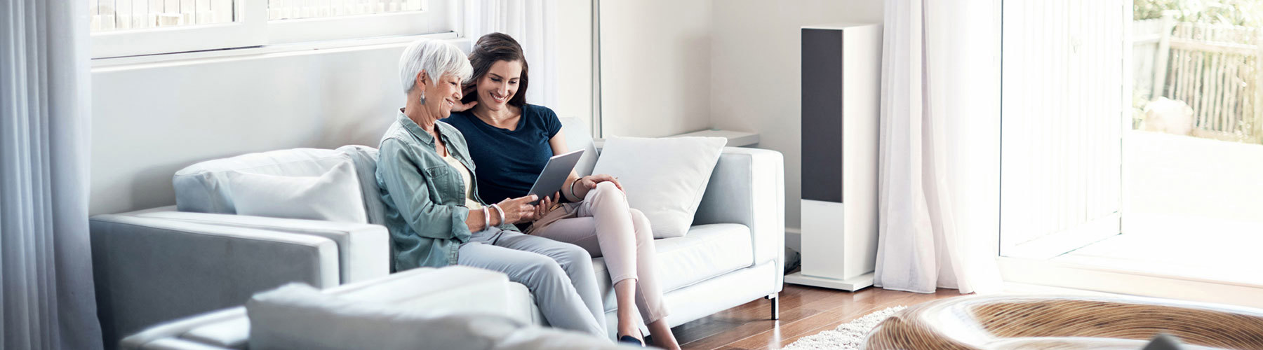 Two women sitting on a couch looking at a tablet